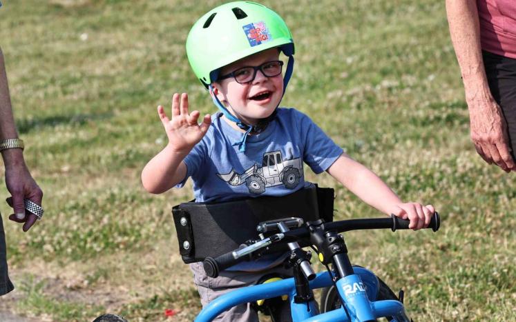 boy on bike waving a camera